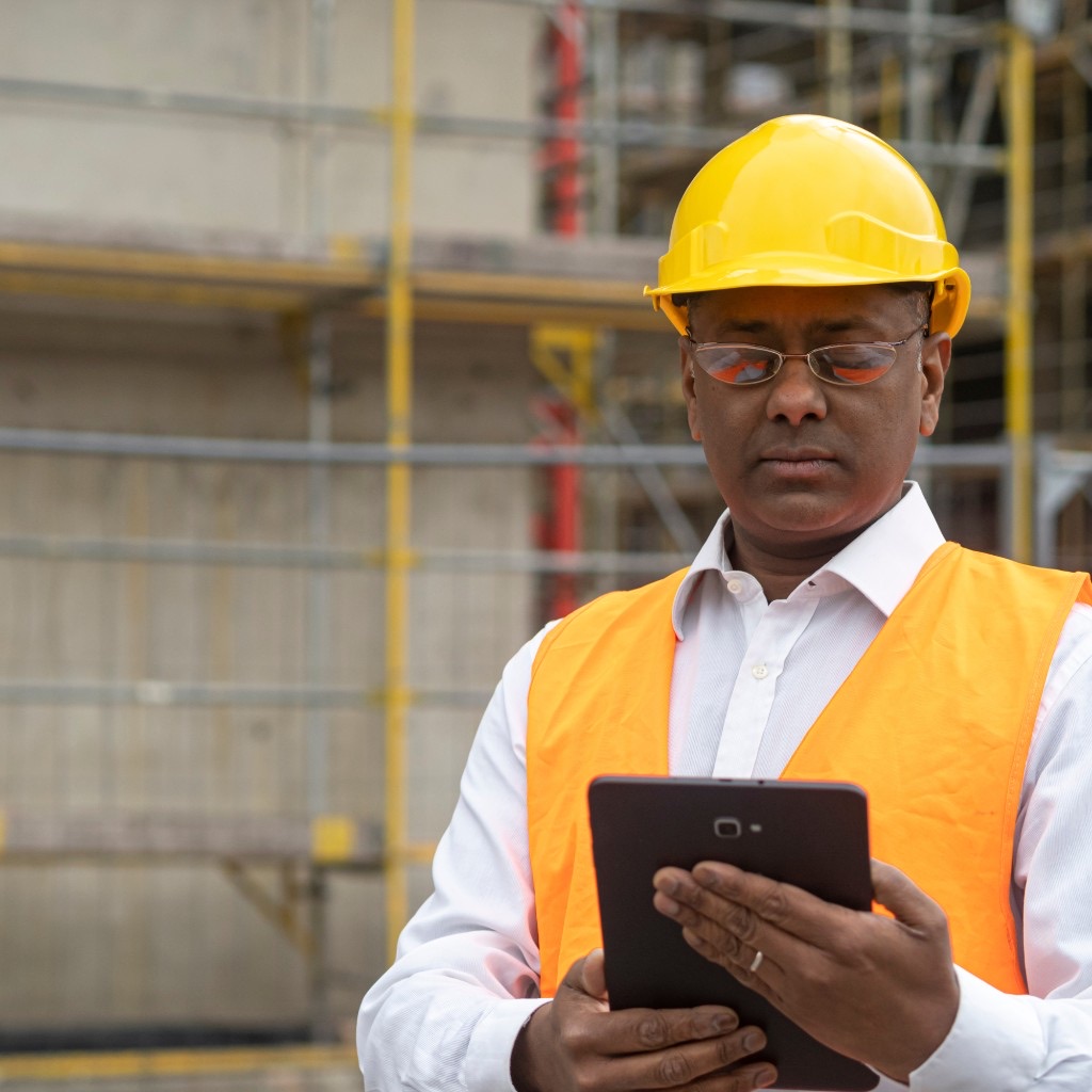 Engineer in a hard hat and safety vest reading a tablet on a job site